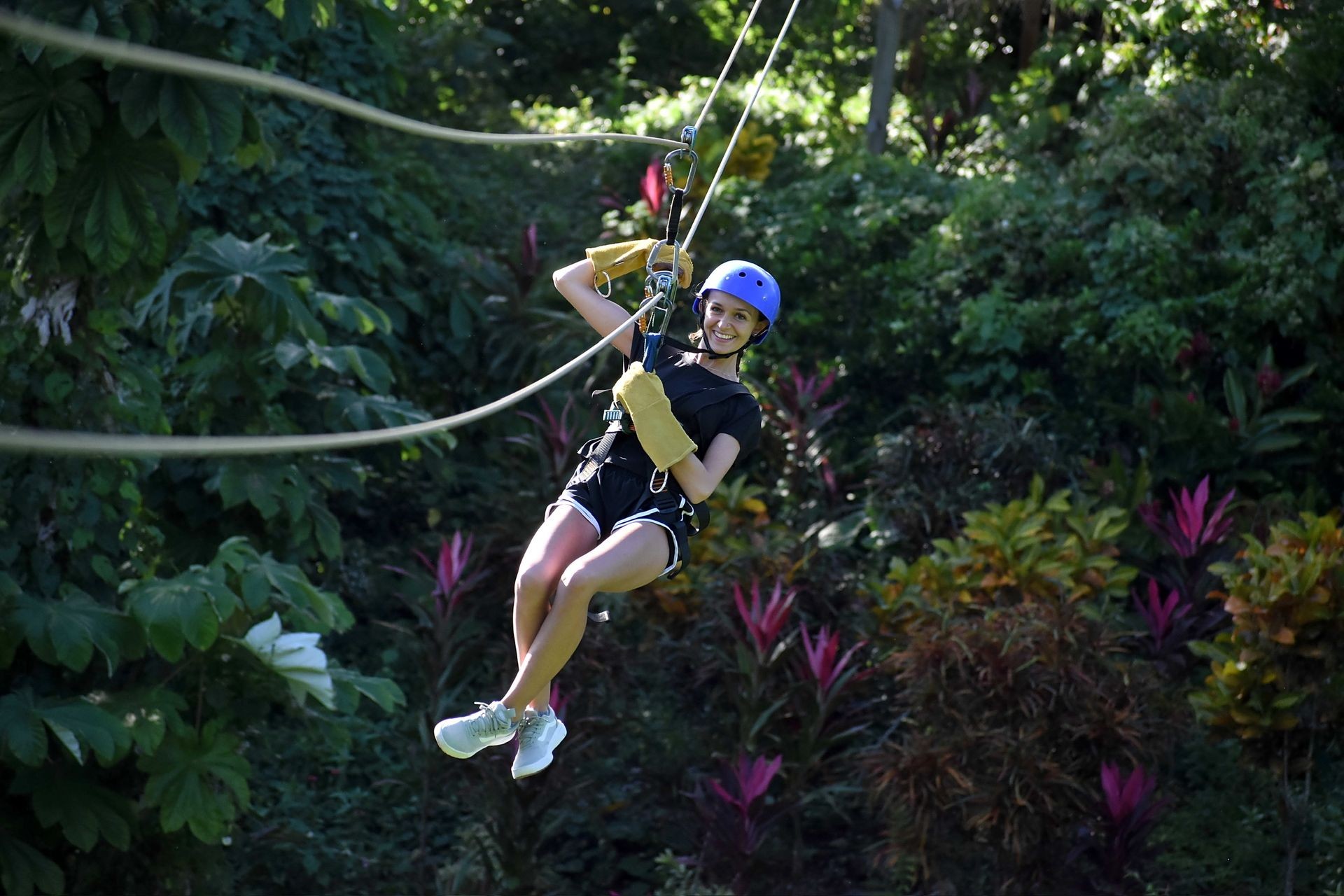 Person ziplining through lush green tropical forest, wearing safety gear and smiling.